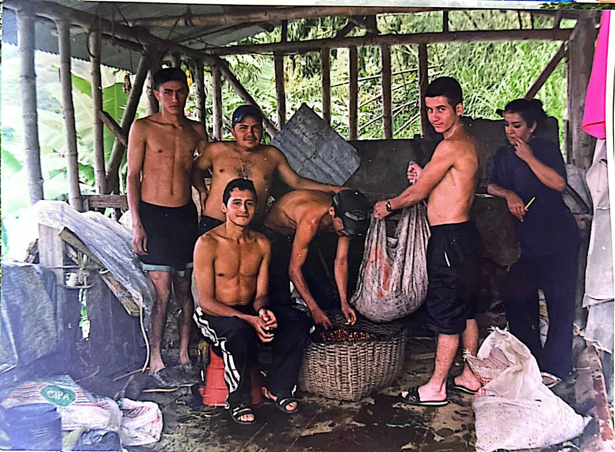 Fotografía antigua: varios jóvenes con canastos de recolección bajo un cobertizo de guadua