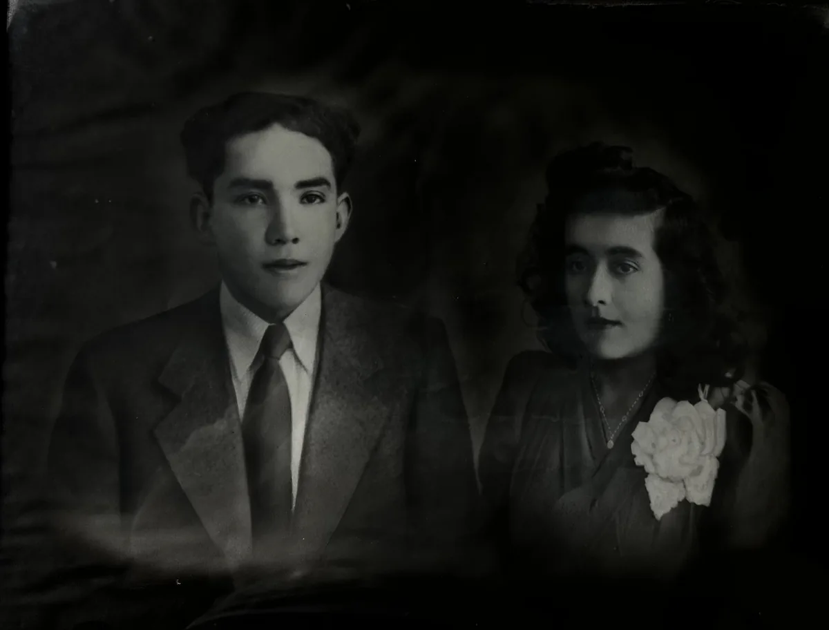 Retrato de estudio antiguo en blanco y negro: una pareja joven, él de traje y corbata, ella con un ramillete de flores claras en el vestido